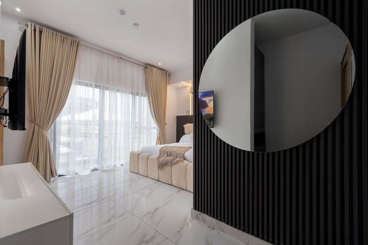 A modern hotel room with a large mirror, a bed, a TV, and a view of the city.