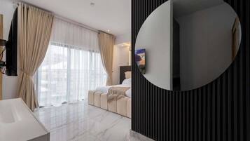 A modern hotel room with a large mirror, a bed, a TV, and a view of the city.
