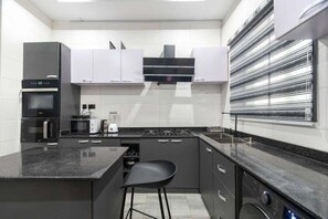 A modern kitchen with a central island, built-in appliances, and a stainless steel backsplash. - Velora Apartment (Owerri)