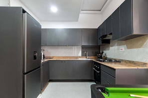 A modern kitchen with dark cabinetry, a stainless steel refrigerator, a countertop with a sink, and a stove.