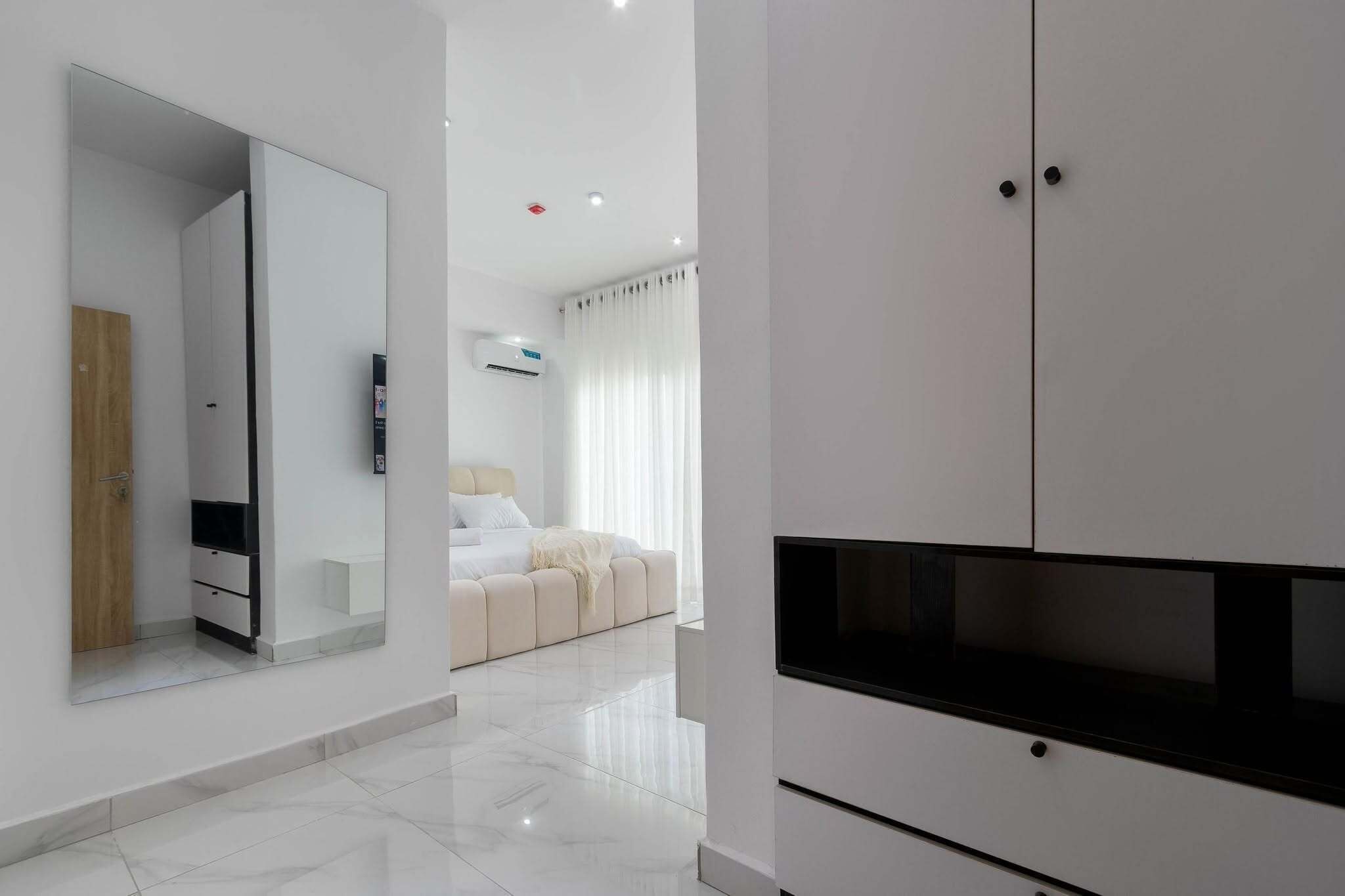 Une chambre d’hôtel moderne dotée d’un grand miroir, d’un téléviseur à écran plat, d’un lit avec une literie blanche et d’une armoire blanche.
