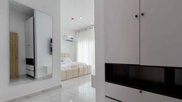 Une chambre d’hôtel moderne dotée d’un grand miroir, d’un téléviseur à écran plat, d’un lit avec une literie blanche et d’une armoire blanche.