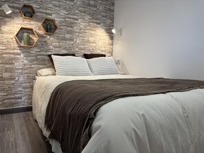 A bedroom with a stone-patterned wall, a bed with white bedding, and three hexagonal wall sconces. - Newly Renovated Apartment with A/C and WiFi in Central Torremolinos (Torremolinos)