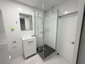 Een moderne badkamer met een douche met glazen wand, een wastafel met spiegel erboven en witte betegelde wanden.