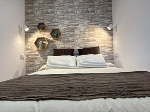 Een slaapkamer met een muur met een stenen patroon, een bed met een gebreide deken en zeshoekige wandlampen.