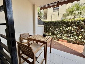 Een terras met een houten tafel en stoelen, een plant in pot en een muur begroeid met begroeiing.