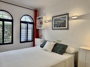 Een slaapkamer met een bed, een raam met uitzicht, een plank met decoratieve items en een lijst met afbeelding aan de muur.