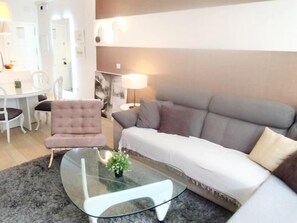 Een moderne woonkamer met een glazen salontafel, een bank en een fauteuil.