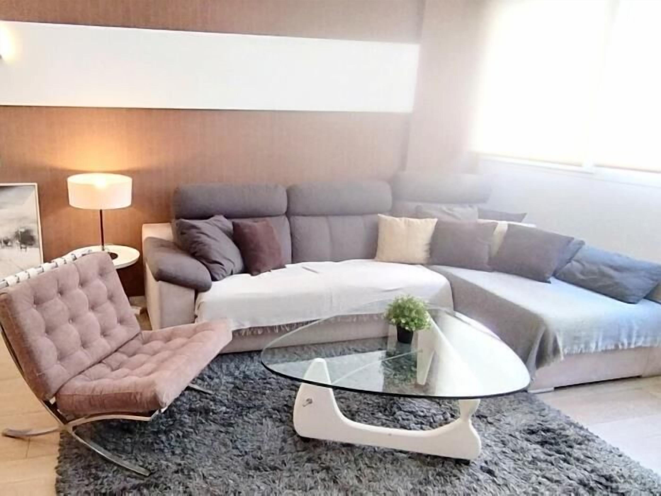 A modern living room with a grey sofa, a tufted armchair, and a glass coffee table.