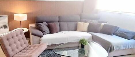 A modern living room with a grey sofa, a tufted armchair, and a glass coffee table.