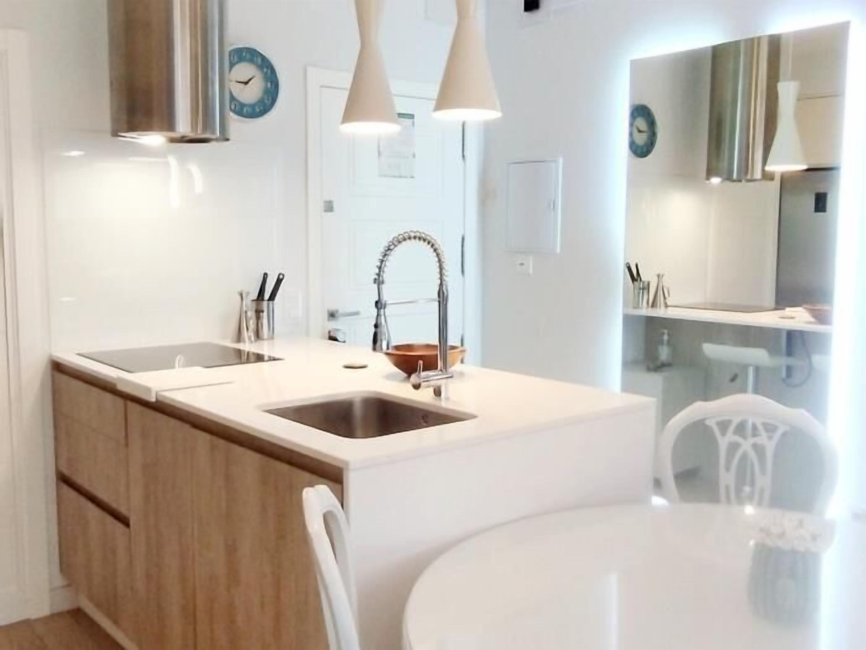Una cocina moderna con una isla central, muebles blancos y lámparas colgantes.