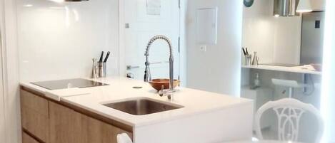 Una cocina moderna con una isla central, muebles blancos y lámparas colgantes.
