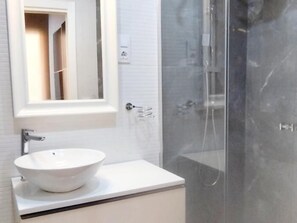 Een badkamer met een witte wastafel, een spiegel en een douchecabine met glazen wanden.