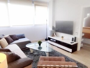 A modern living room with a sofa, a glass coffee table, a flat-screen TV, and a small plant. - One-Bedroom Apartment by La Nogalera Square in Central Torremolinos (Torremolinos)