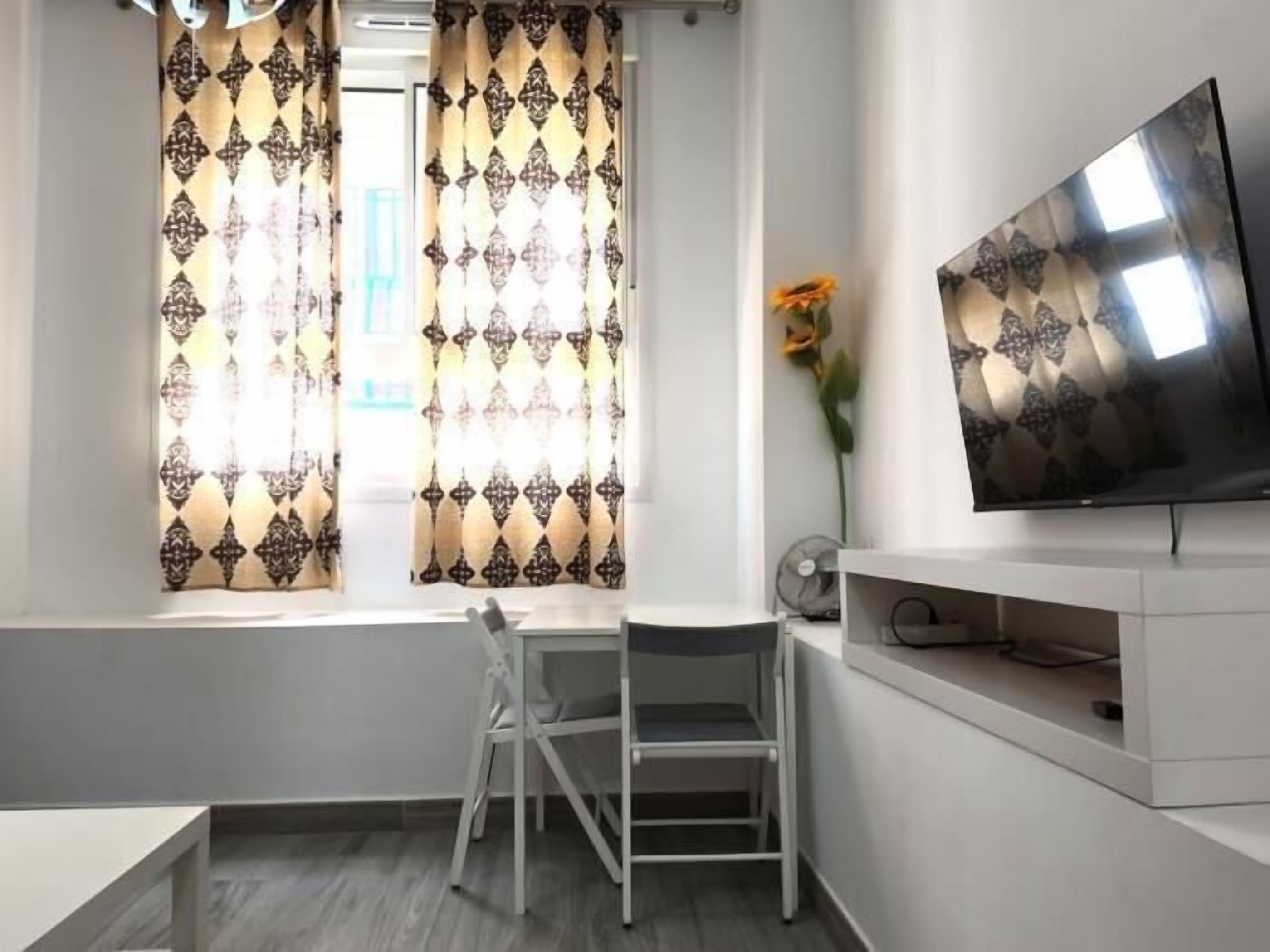 Ein modernes Zimmer mit Schreibtisch, Stuhl, Fernseher und Vorhängen.