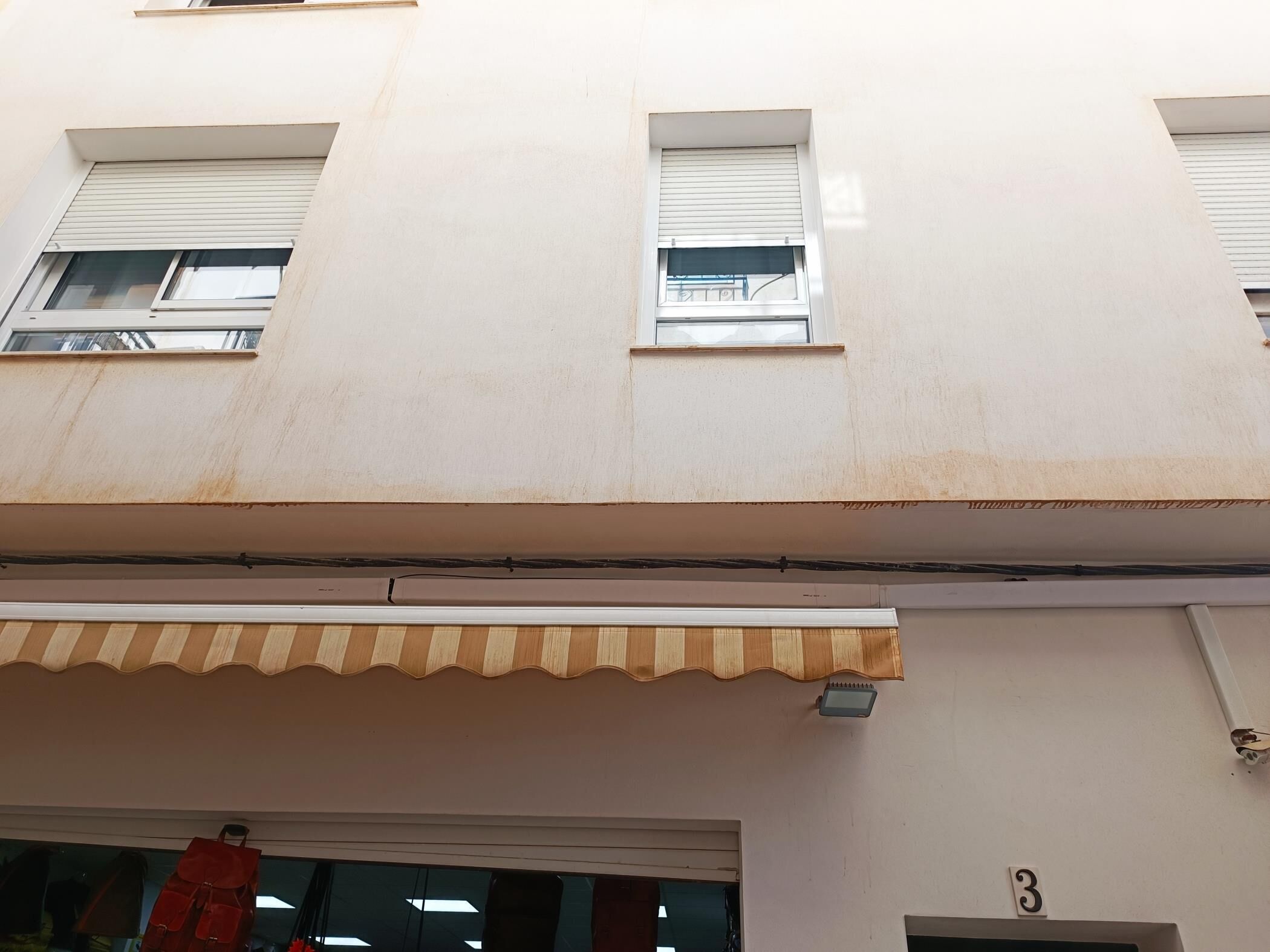 Ein Gebäudefassaden mit drei Fenstern, ein Schaufenster mit Markise und die Hausnummer 3.