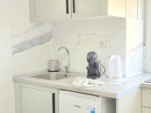 Eine Küche mit Marmor-Spritzschutz, einem Waschbecken mit Wasserhahn, einem Wasserkocher und einem Geschirr-Abtropfgestell.