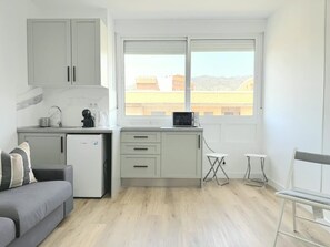 Ein kompakter Wohnbereich mit Küchenzeile, einem grauen Sofa, einem Esstisch und einem Fenster mit Blick auf die Stadt.