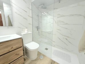 A bathroom with a glass-enclosed shower, a white toilet, a wooden vanity, and a marble backsplash.