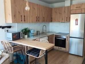 Een moderne keuken met houten kastjes, een ingebouwde oven, een koelkast en een eethoek met stoelen.