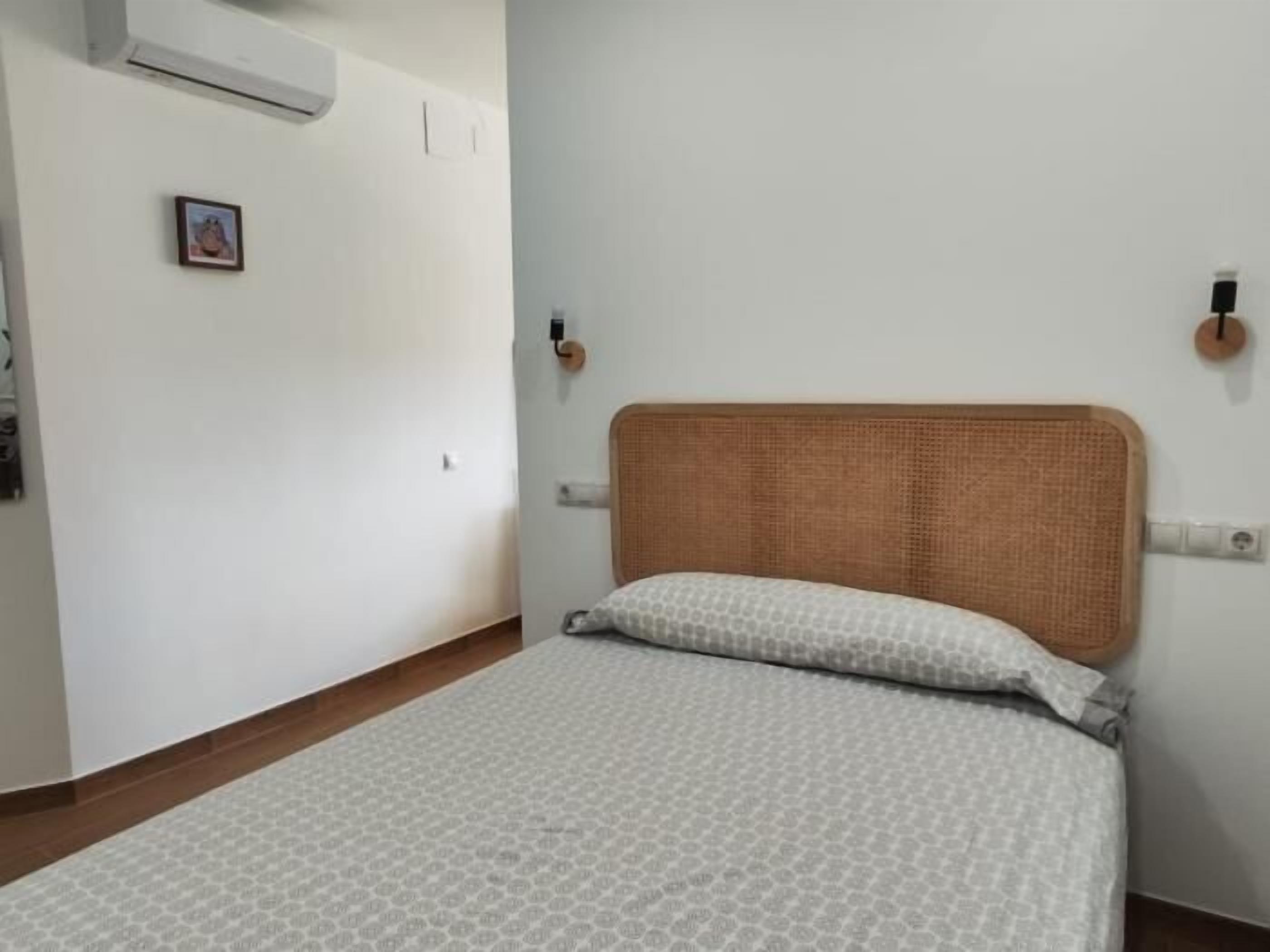 Une chambre avec un lit simple, des murs blancs, un plancher en bois et un petit tableau accroché au mur.