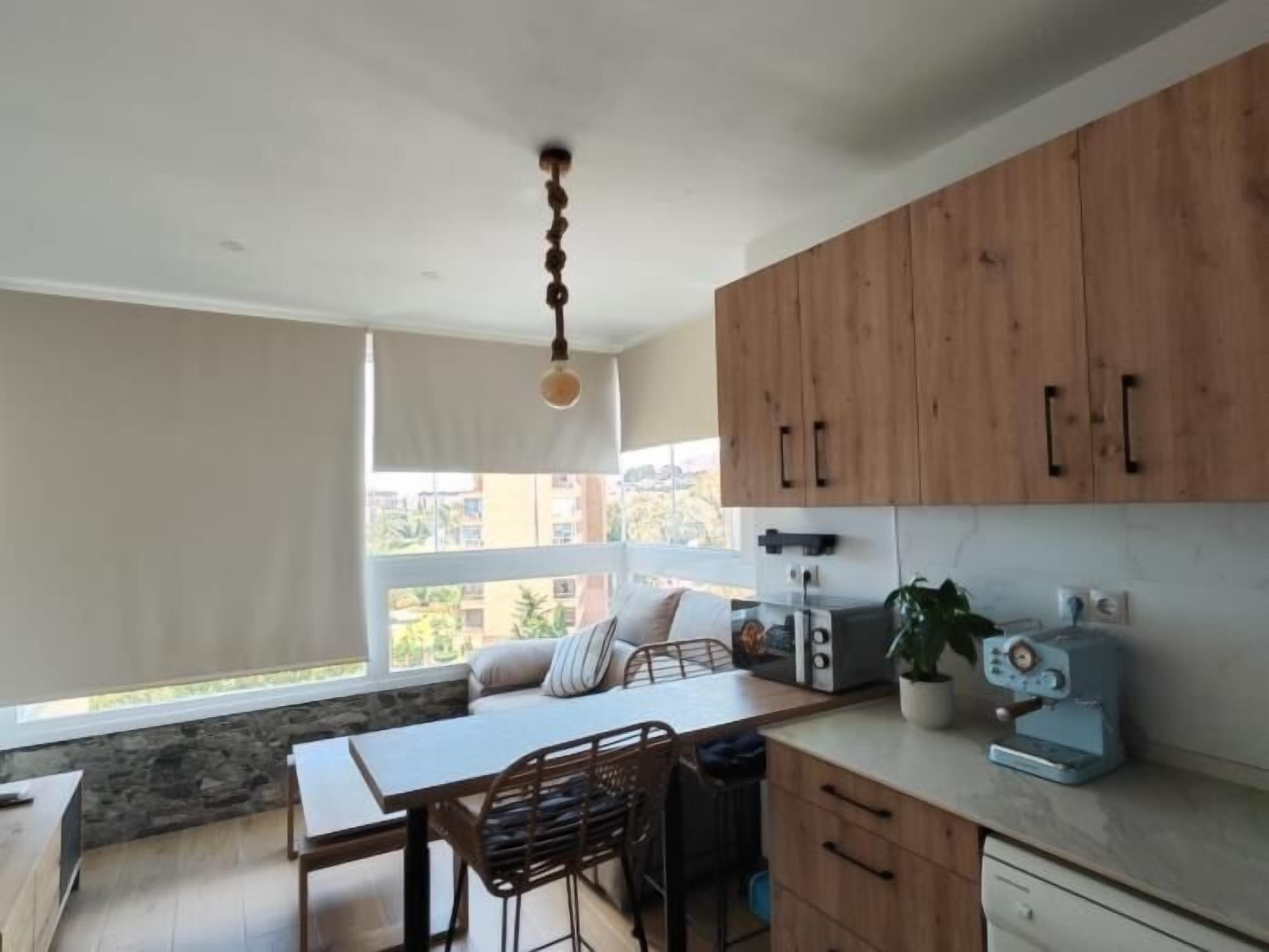 Una cocina moderna con armarios de madera, un comedor con mesa y sillas, y un amplio ventanal con vistas al exterior.