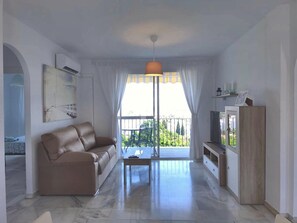 A living room with a sofa, a coffee table, a TV, and a balcony with a view. - Two-Bedroom Apartment with Terrace and Sea Views near the Centre (Torremolinos)