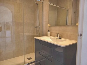Een moderne badkamer met een glazen douchecabine, een wit wastafelmeubel en een spiegel erboven.