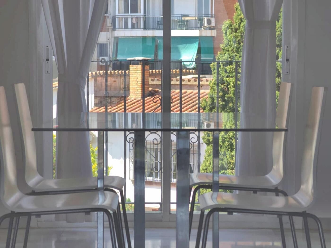 A balcony with a glass railing, two white chairs, and a view of a building with a green awning.