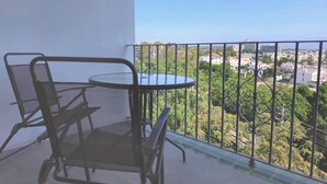 Varanda com mesa redonda e duas cadeiras, vista para paisagem urbana com áreas verdes e edifícios.