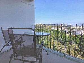 Een balkon met een ronde tafel en twee stoelen, met uitzicht op een stadslandschap met groen en gebouwen.