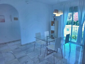 Een moderne eetruimte met een glazen tafel en stoelen, een hanglamp en uitzicht op een balkon met een hekwerk.
