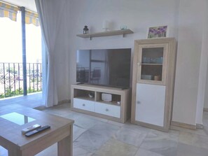 Ein Wohnzimmer mit Flachbildfernseher, Holzschrank und Balkon mit Geländer.