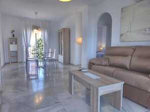 A modern living room with a brown sofa, a wooden coffee table, and a dining area with chairs and a table. - Two-Bedroom Apartment with Terrace and Sea Views near the Centre (Torremolinos)