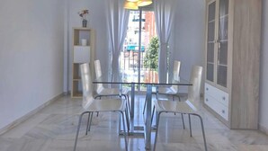 Uma sala de jantar com mesa e cadeiras de vidro, um armário de madeira e vista para o exterior.