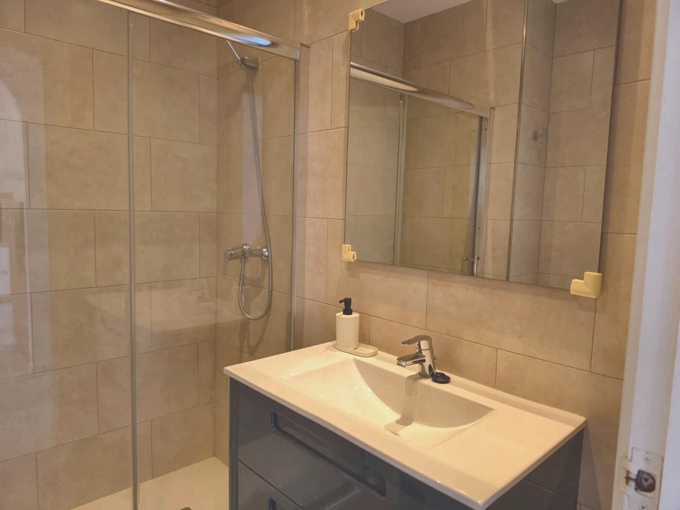 A bathroom with a glass-enclosed shower, a white sink, and a mirror.