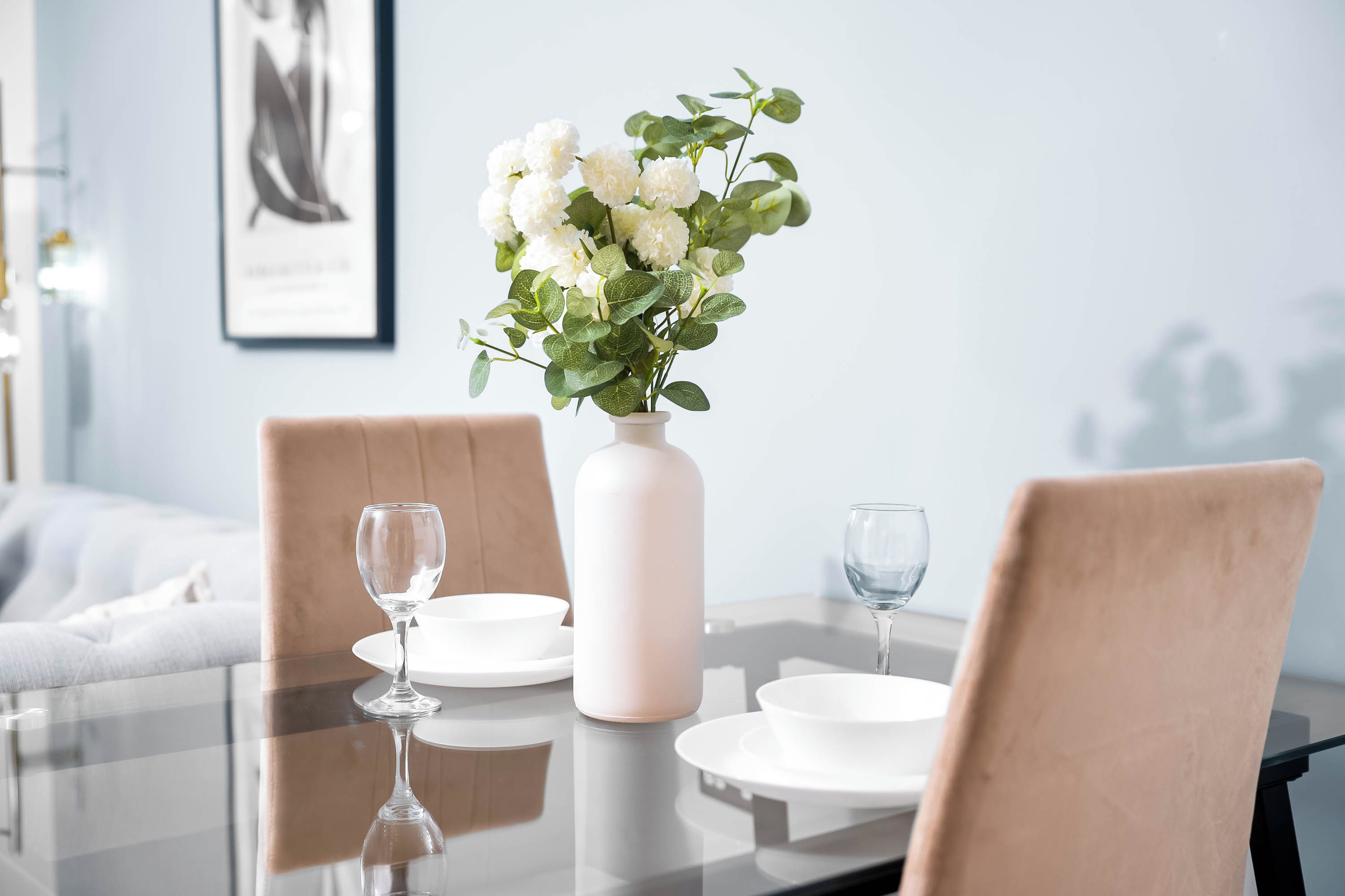 A dining table with a vase of flowers, two wine glasses, and white plates.