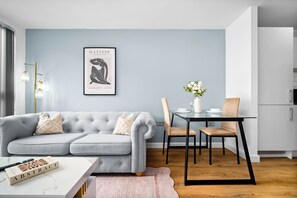 Un salon moderne avec un canapé gris, une table à manger avec des chaises et un coin cuisine.