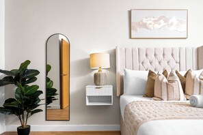 Ein Schlafzimmer mit einem Bett, einem Nachttisch mit Lampe, einem Spiegel und einem gerahmten Kunstwerk an der Wand.