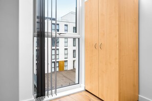 Une pièce avec une armoire en bois, une porte-fenêtre coulissante et une vue sur un bâtiment à l’extérieur.