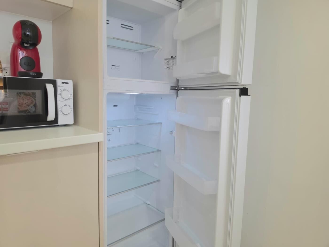 Une cuisine équipée d’un four à micro-ondes, d’un réfrigérateur et d’un appareil de couleur rouge posé sur le plan de travail.