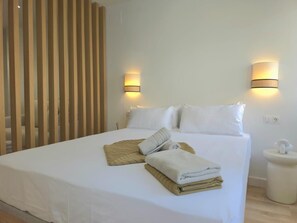 A neatly made bed with white linens and a folded towel, two wall-mounted lamps, and a wooden slat partition. - Renovated Studio with Pool and Terrace, 7 Minutes from Bajondillo Beach (Torremolinos)