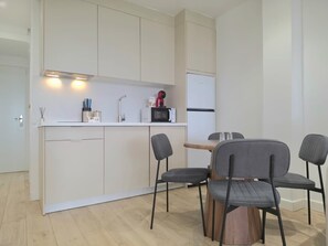 A modern kitchen with white cabinets, a microwave, and a refrigerator. There are two chairs and a small wooden table. - Renovated Studio with Pool and Terrace, 7 Minutes from Bajondillo Beach (Torremolinos)