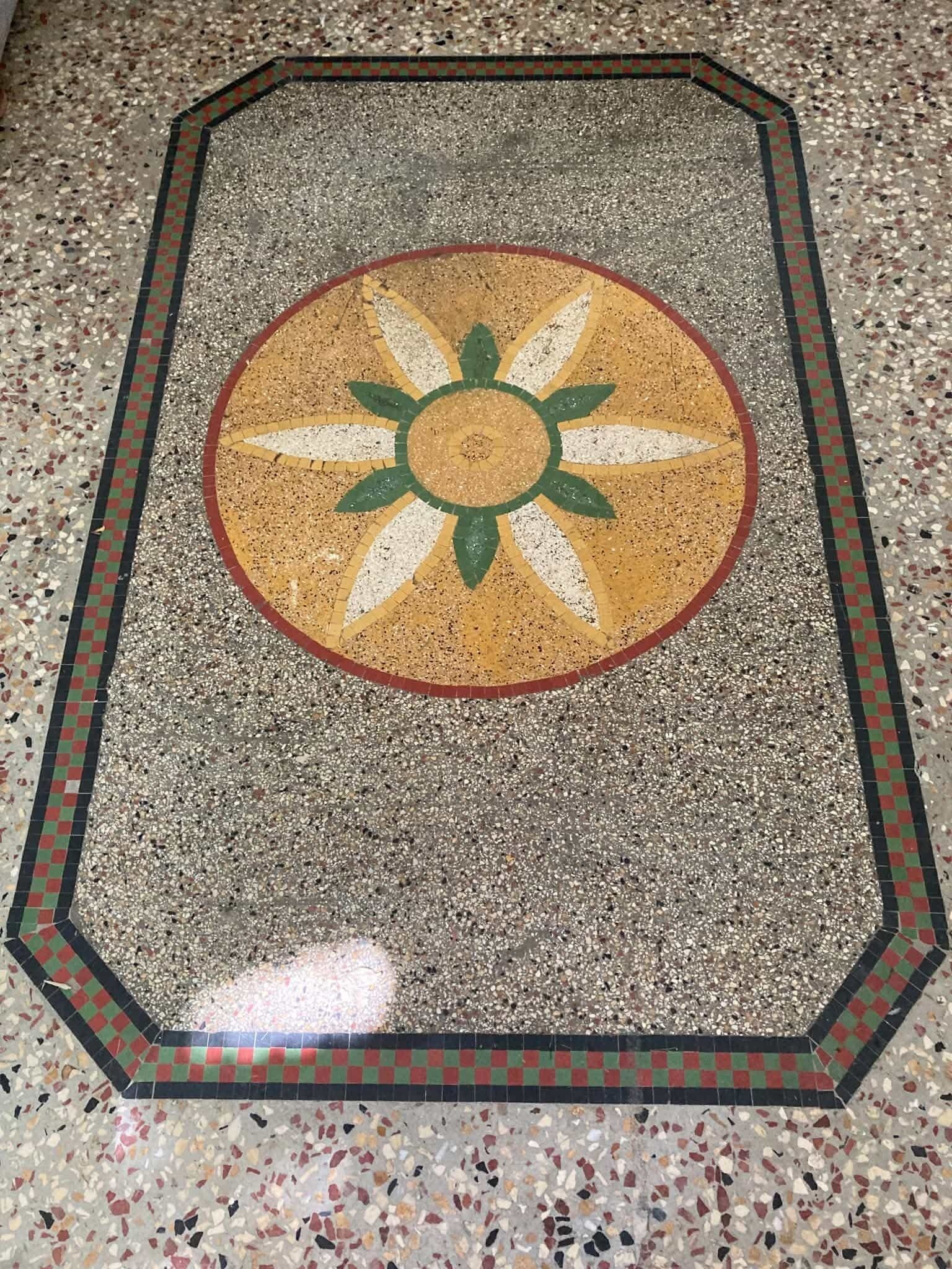 Et terrazzogulv med et centralt cirkulært design med en sol.