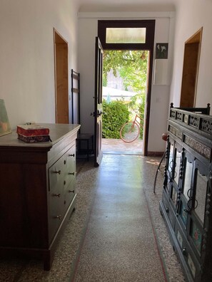A hallway with a wooden cabinet, a bicycle outside, and a door leading to a garden. - One of a kind! In a Provençal village, a spacious apartment with access to our bookstore (Courthézon)