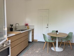 A compact kitchen with a sink, countertop, and wooden cabinets. There is a dining area with a round table and two chairs. - In a Provençal village, a spacious apartment with access to our bookstore (Courthézon)