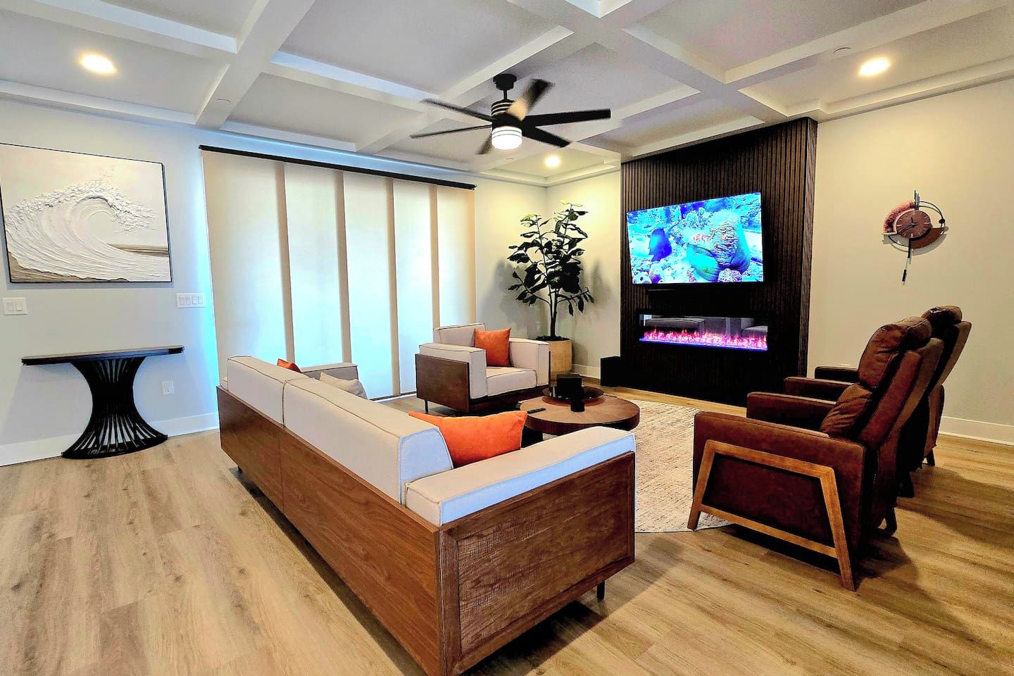 Een moderne woonkamer met een bank, een fauteuil, een televisie en een plafondventilator.