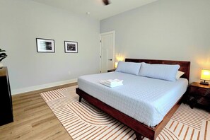 A neatly made bed with a white duvet and pillows, a wooden headboard, a striped rug, and two framed pictures on the wall. - Brand New Beach House | Sleeps 8 | Ocean Pines, MD (Berlin)