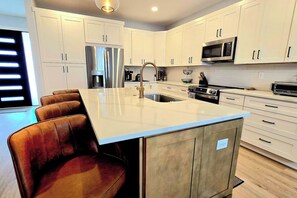 A modern kitchen with white cabinets, stainless steel appliances, and a central island with seating. - Brand New Beach House | Sleeps 8 | Ocean Pines, MD (Berlin)