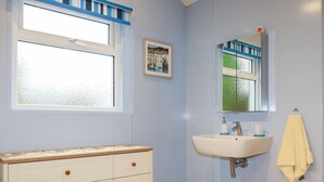 Un baño con tocador blanco, lavamanos, espejo, ventana y toallero.